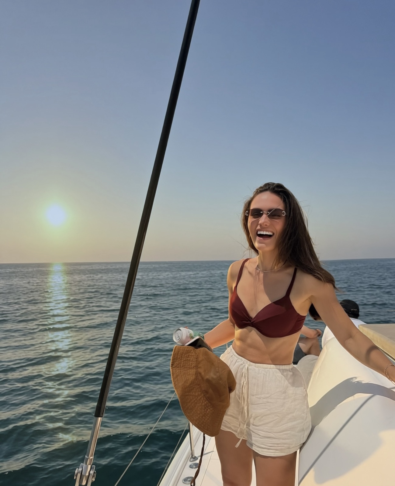 Tay laughing on the deck of a boat at sunset, with the sun low over the water
